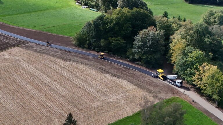 Detailausschnitt: Asphaltfertiger mit Lkw beim Einbau des Asphalts am Agrarweg Reiting-Kiriau, dahinter zwei Walzen