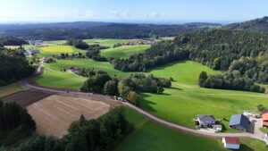 Luftaufnahme des neu asphaltierten Agrarweges Reiting-Kiriau zwischen Feldern und Wiesen, rechts im Vordergrund ein Bauernhof
