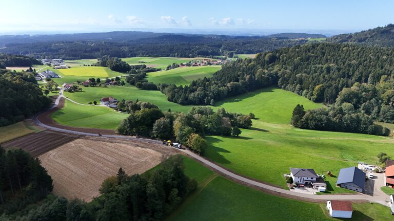 Luftaufnahme des neu asphaltierten Agrarweges Reiting-Kiriau zwischen Feldern und Wiesen, rechts im Vordergrund ein Bauernhof