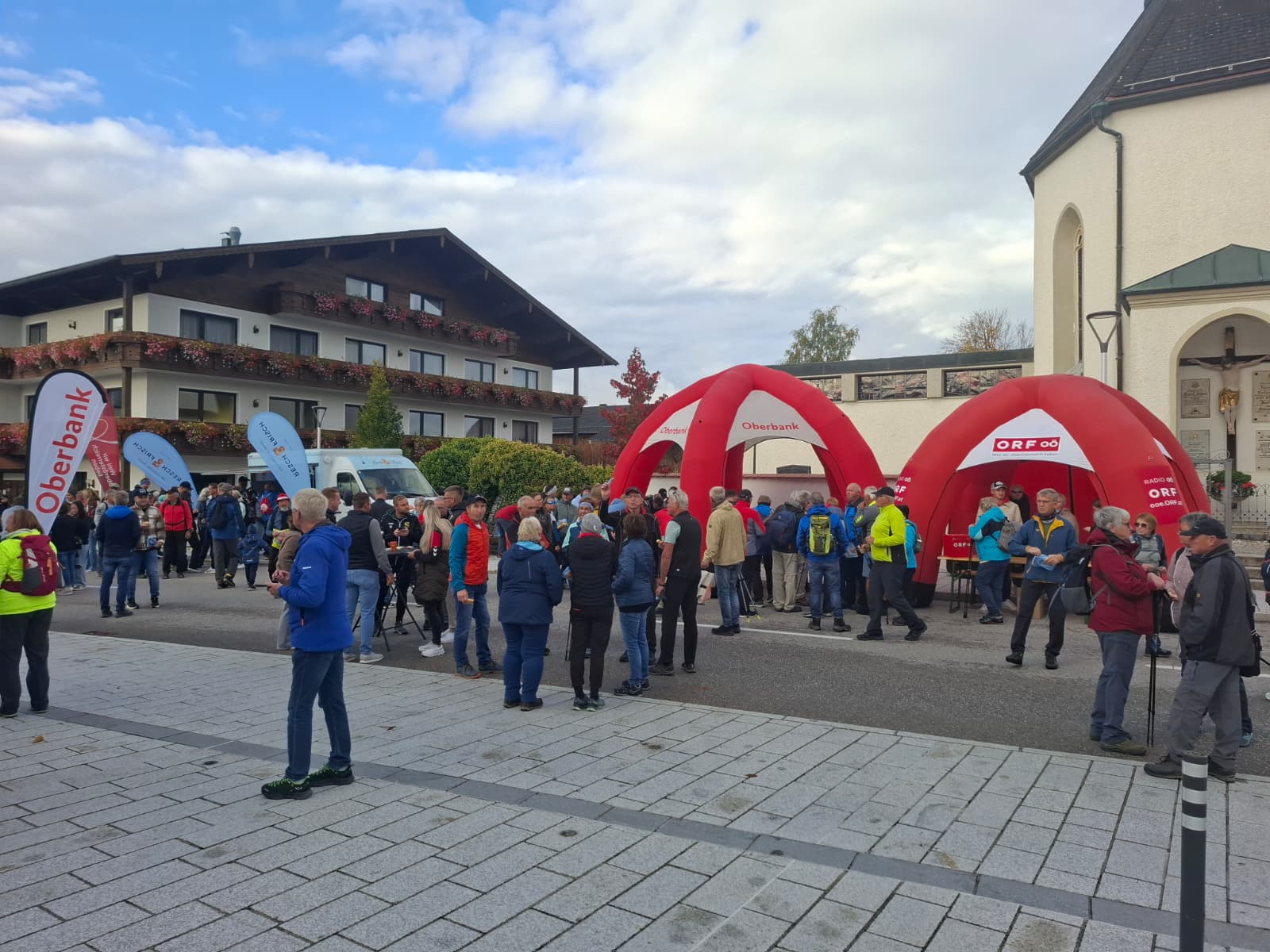 Wanderinnen und Wanderer beim Start des ORF-Wandertags am Ortsplatz von St. Aegidi mit roten ORF-Zelten neben der Pfarrkirche